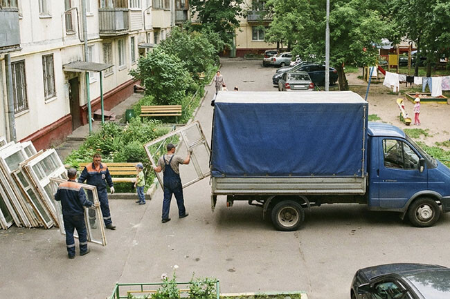 Грузчики у подъезда вывозят старые окна Газелью