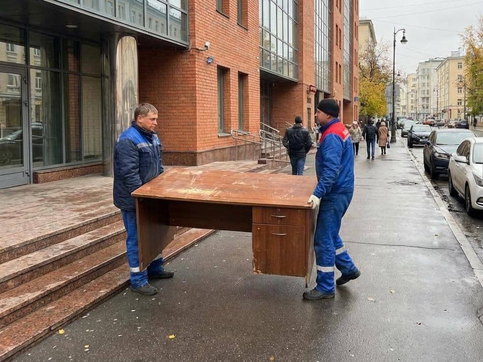 Грузчики вывозят старый стол из офиса