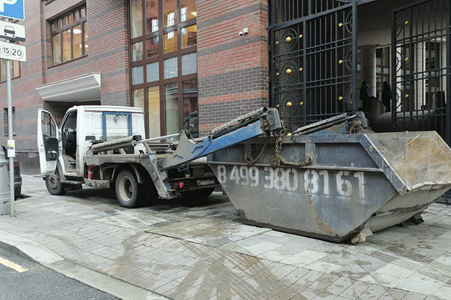 Мусоропогрузчик с контейнером на улице в Москве